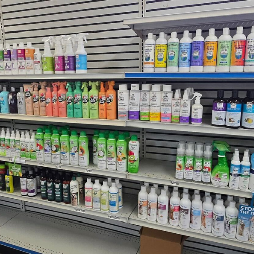 Shelves stocked with various pet cleaning products in bottles of different colors and sizes. Labels indicate diverse brands and types, giving a tidy, organized look.