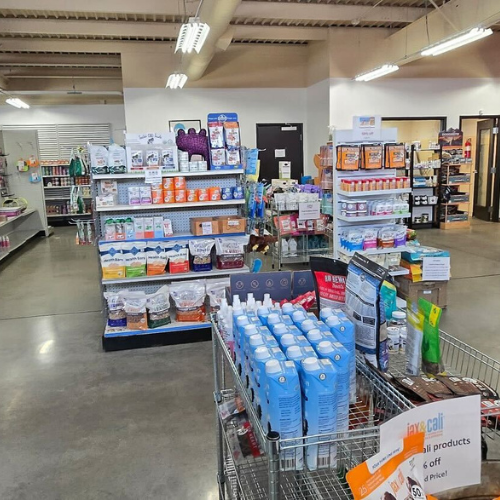 Store interior with neatly arranged shelves displaying pet supplies, including food, grooming products, and accessories. Bright lighting creates a welcoming atmosphere.