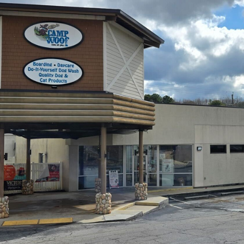 The image shows the exterior of Camp Woof, a pet care facility with a sign advertising boarding, daycare, DIY dog wash, and pet products. The tone is welcoming.