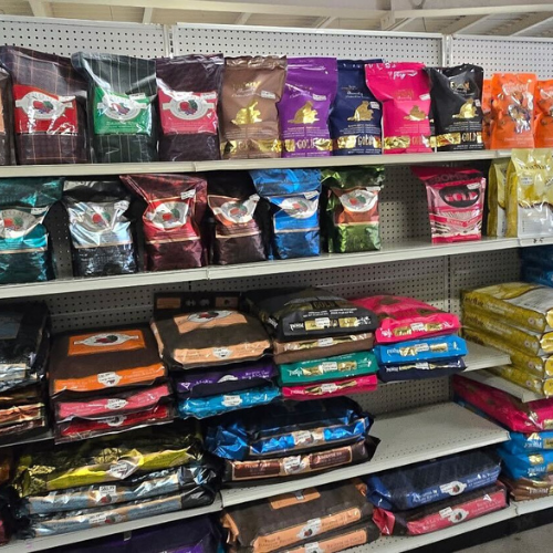 Rows of colorful dog food bags are neatly arranged on store shelves, showcasing various brands and flavors. The vibrant packaging creates a lively display.