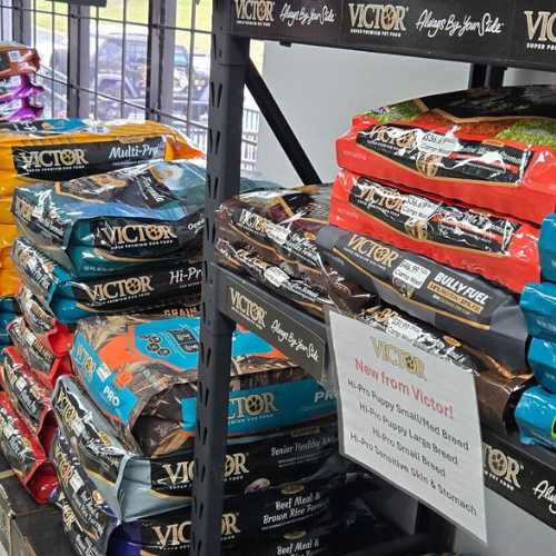 Shelves filled with colorful bags of Victor pet food, each labeled with different formulas. A sign highlights new offerings for small and large breeds.