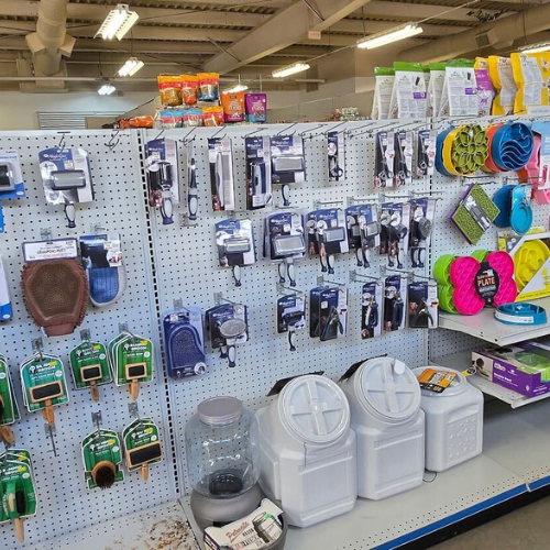A store aisle displays pet grooming tools and supplies on a pegboard. Items include brushes, clippers, and treat bags, creating an organized, vibrant scene.