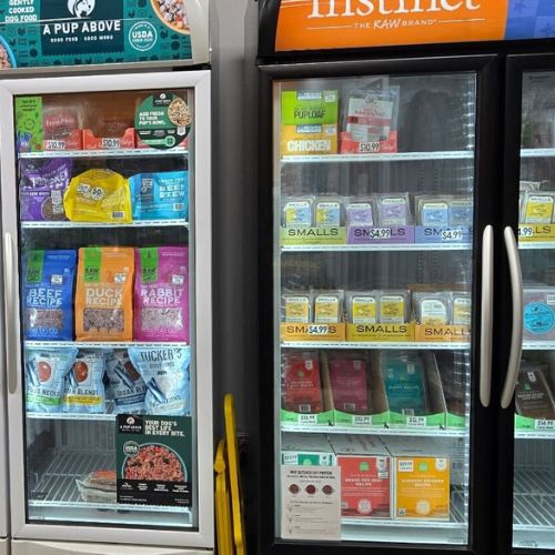 Two grocery store freezers filled with various pet food products. Bright packaging includes brands like 